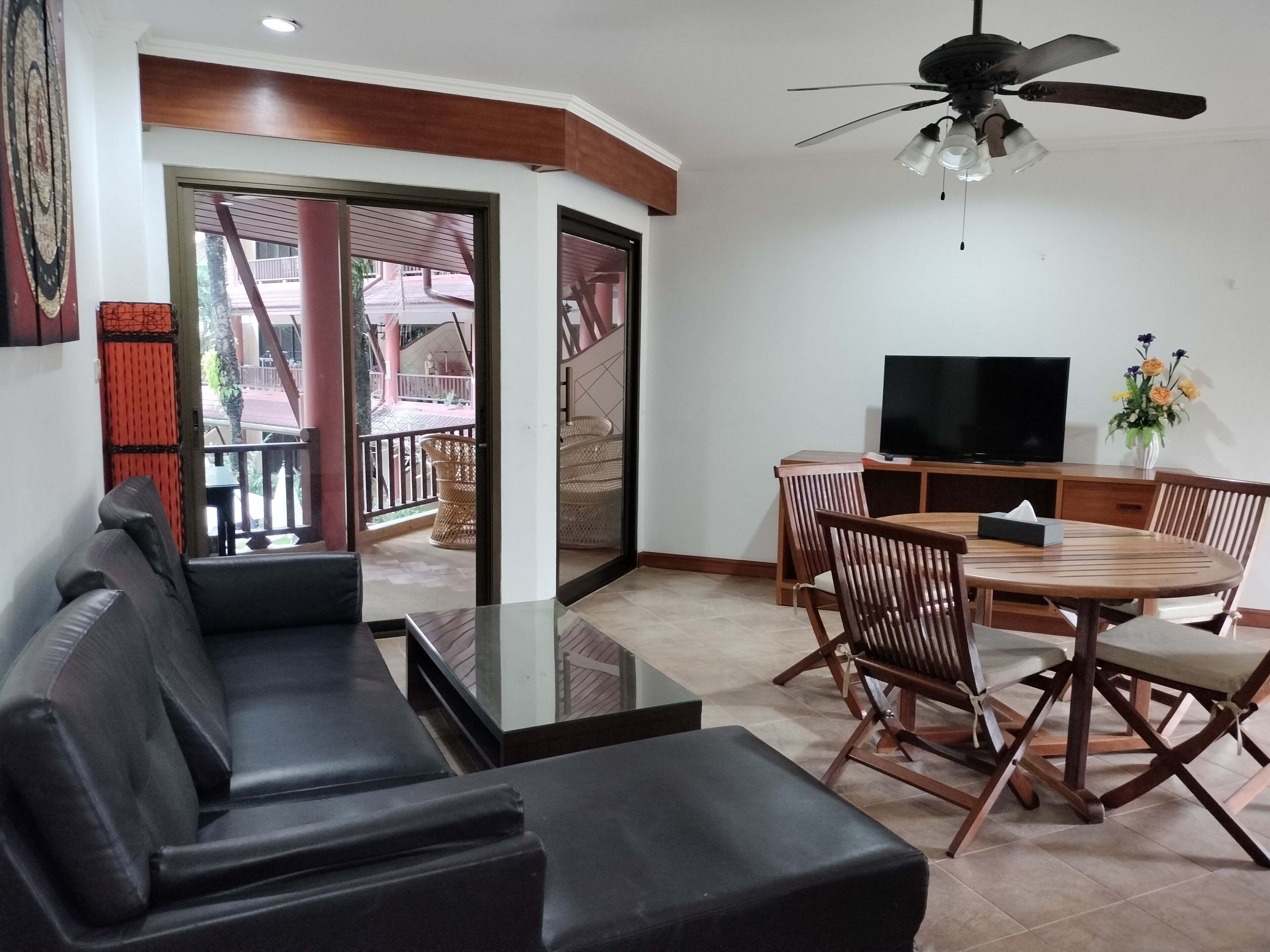 A living room with a sofa, a dining table with chairs, a TV, and a ceiling fan.