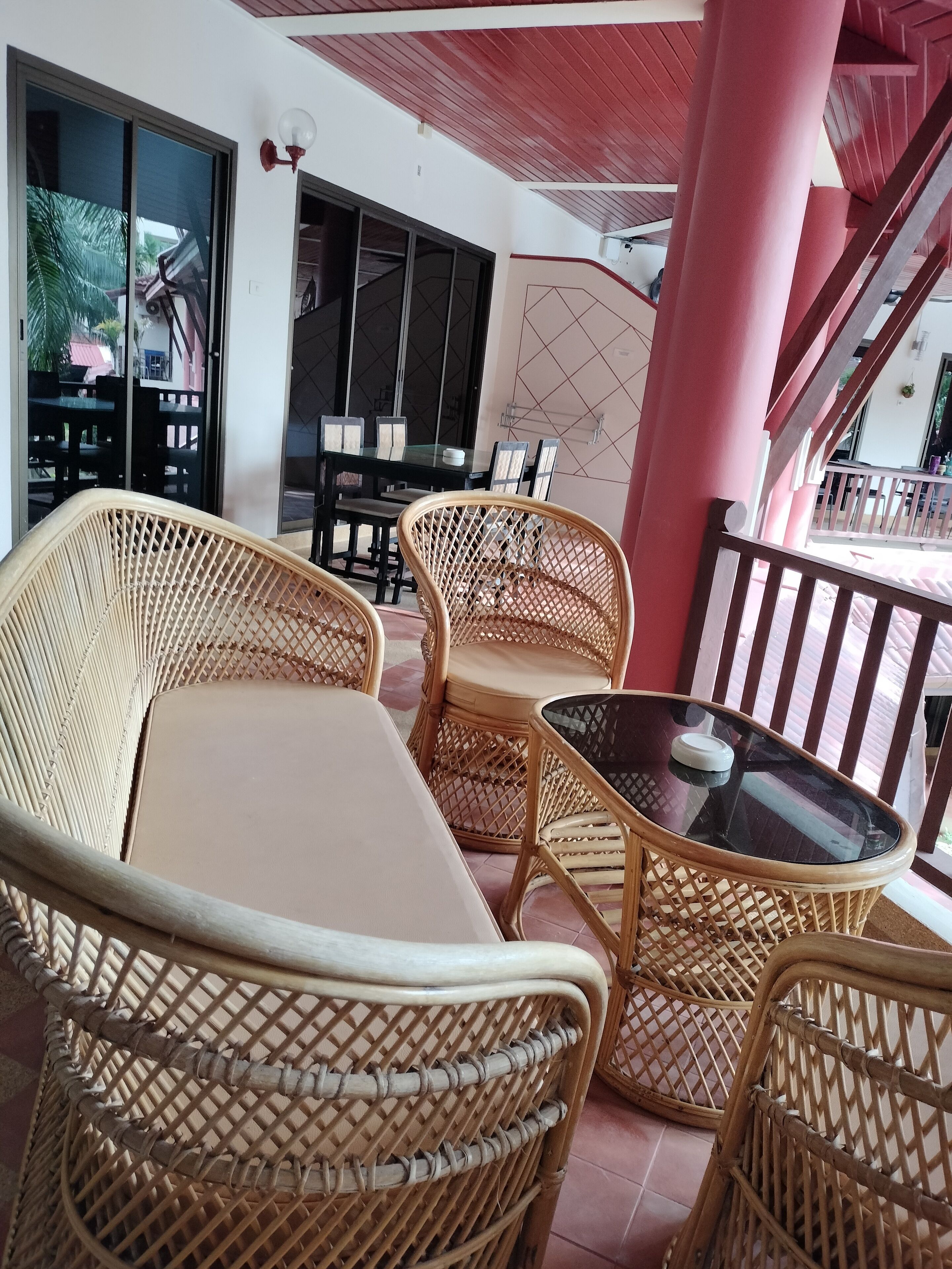 A covered outdoor seating area with wicker furniture and a glass table.