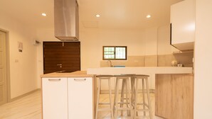 Une cuisine moderne avec des meubles blancs, un plan de travail en bois et trois tabourets de bar.