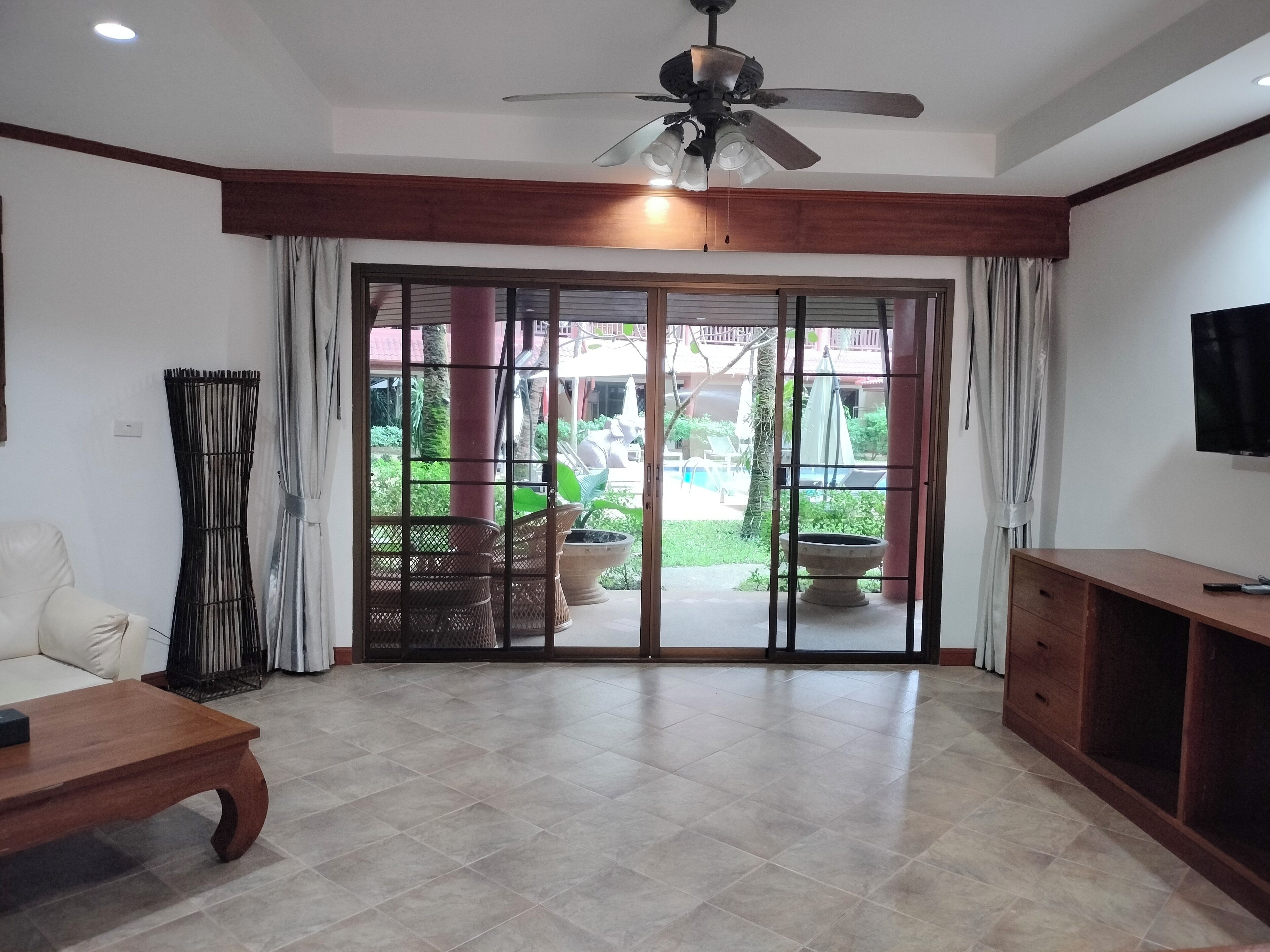 A spacious room with a ceiling fan, a sliding glass door leading to an outdoor area, a wooden coffee table, and a TV on a wooden stand.