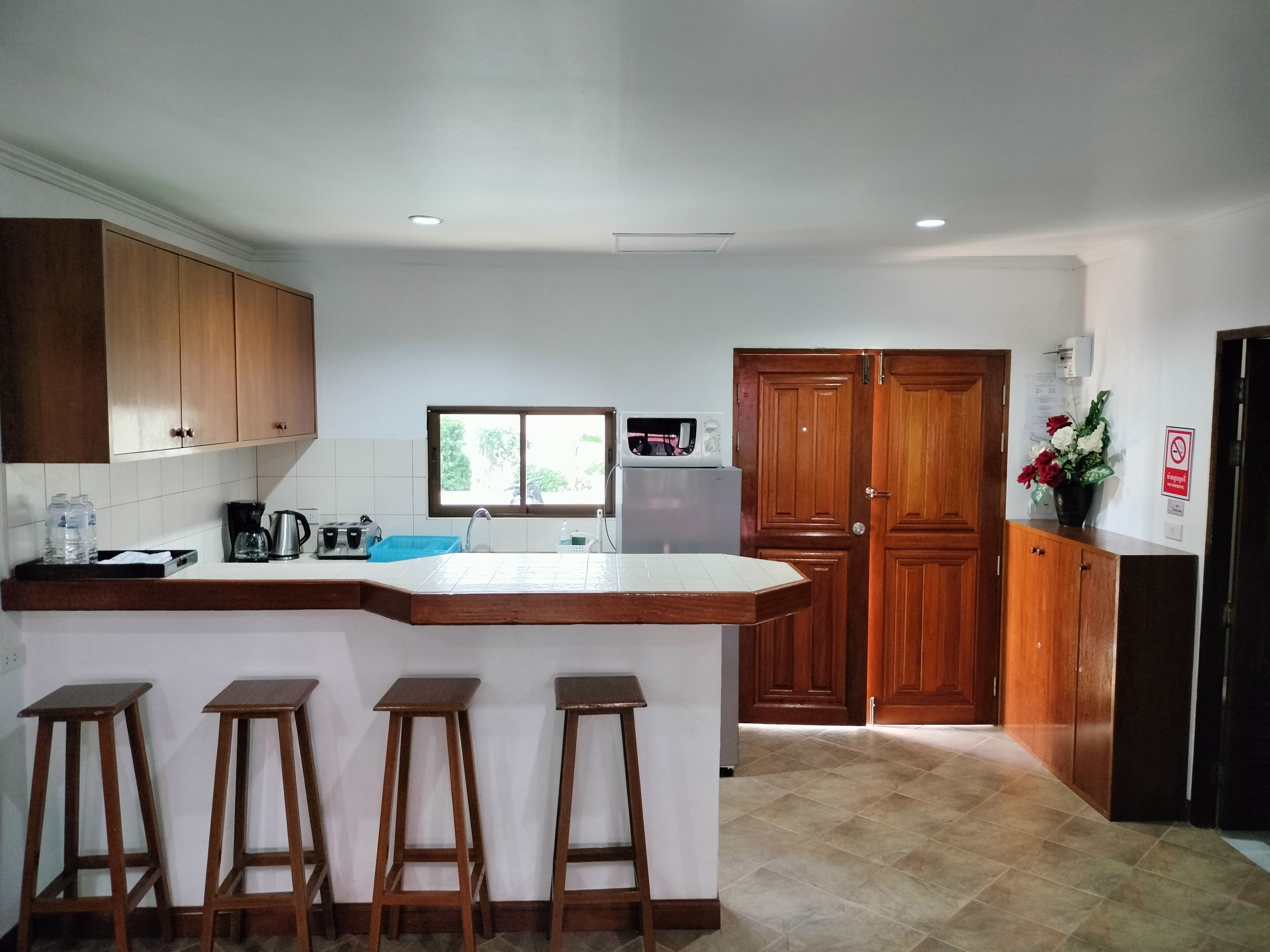 A kitchen with wooden cabinets, a built-in island with stools, a window, and a microwave.
