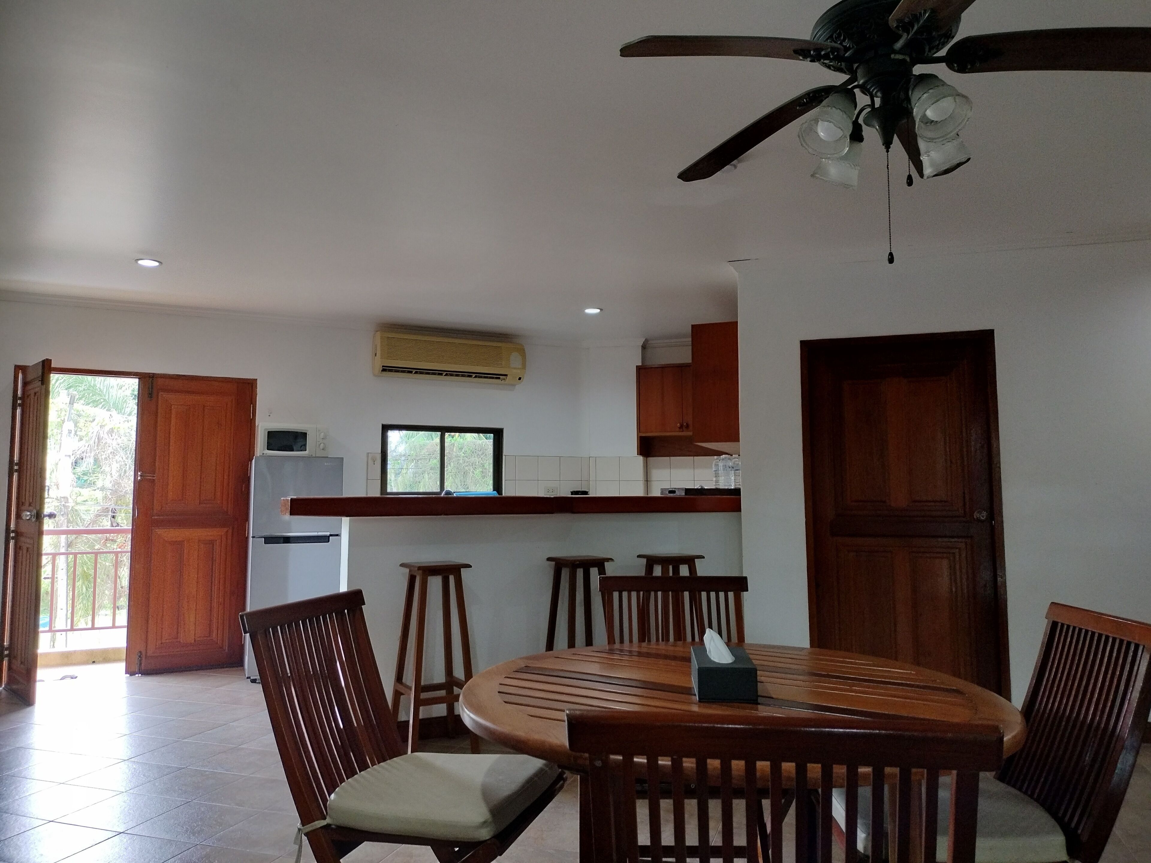 Zona pranzo con tavolo e sedie in legno, una ventola a soffitto e una cucina sullo sfondo.