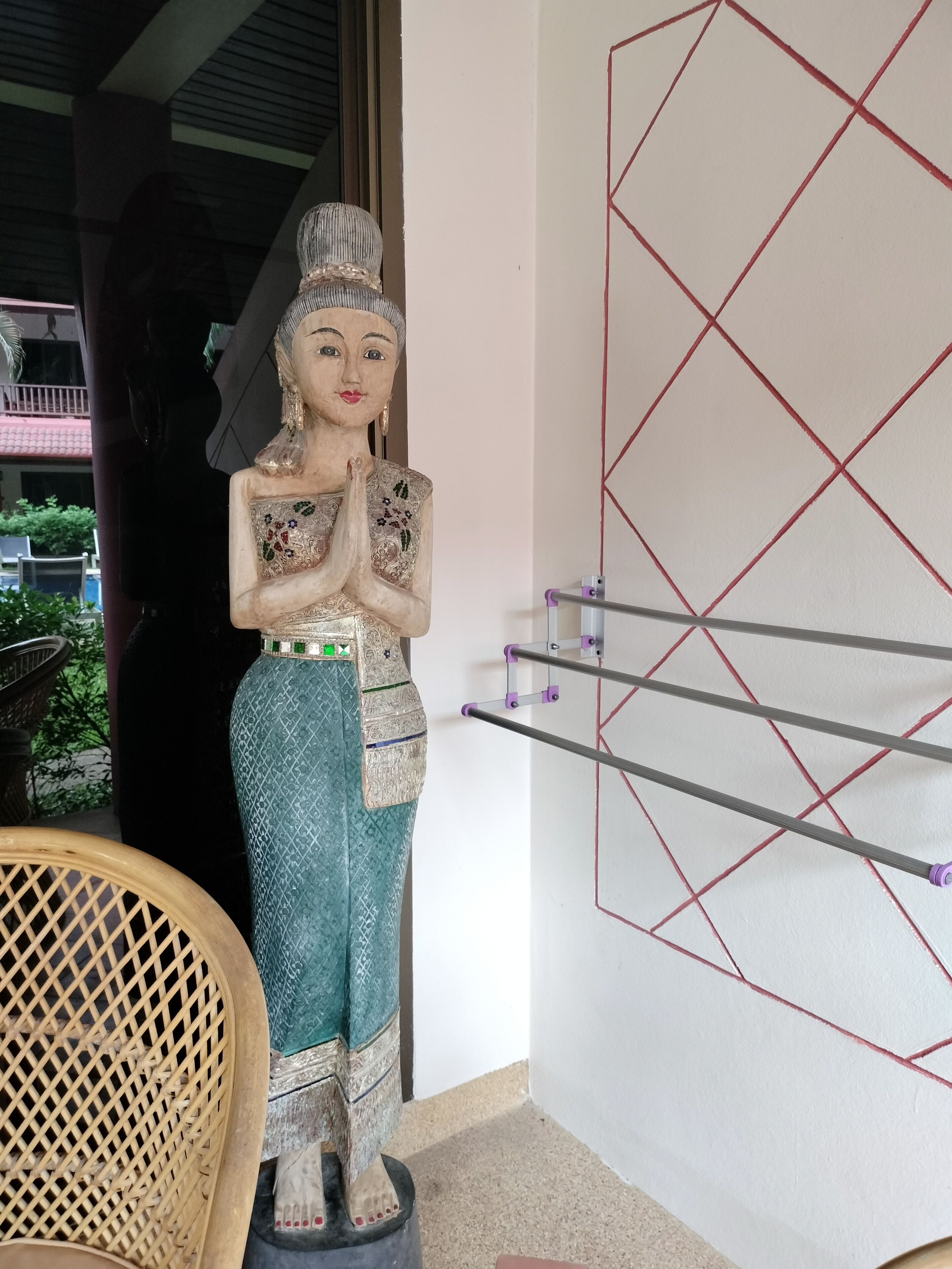 A statue of a woman in traditional attire on a pedestal, a chair, and a wall with geometric patterns.