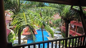 Une vue d’une piscine entourée de palmiers, avec un bâtiment à toit rouge en arrière-plan.