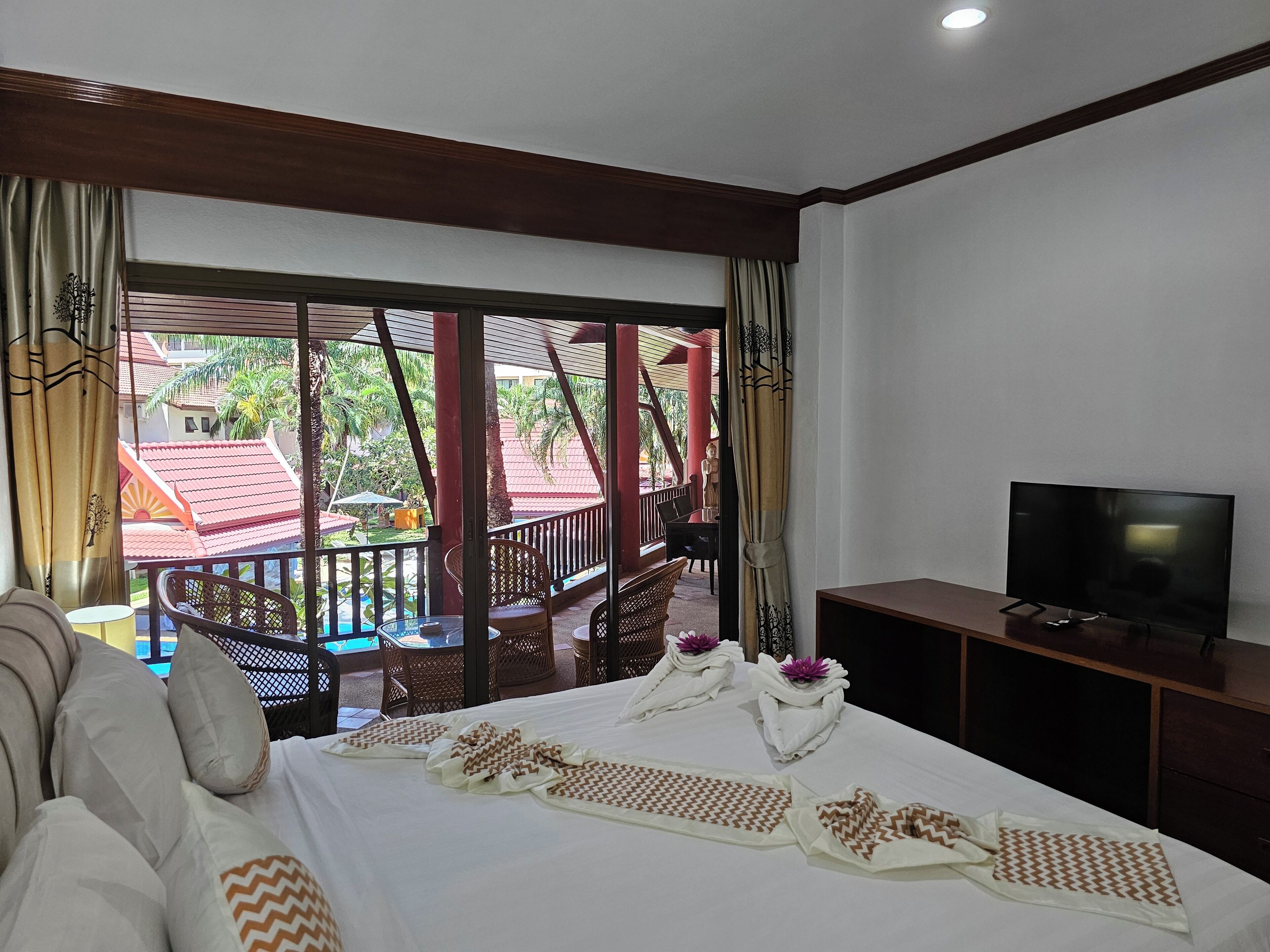 Habitación de hotel con cama, televisión y balcón con vistas a edificios y palmeras.