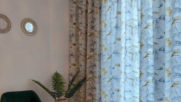 Un salon avec un fauteuil vert, une table ronde en bois ornée de plantes en pot et un rideau à motifs.