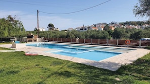 Une piscine rectangulaire, avec une bouée de sauvetage sur le côté droit, entourée d’une pelouse et d’une clôture en bois.