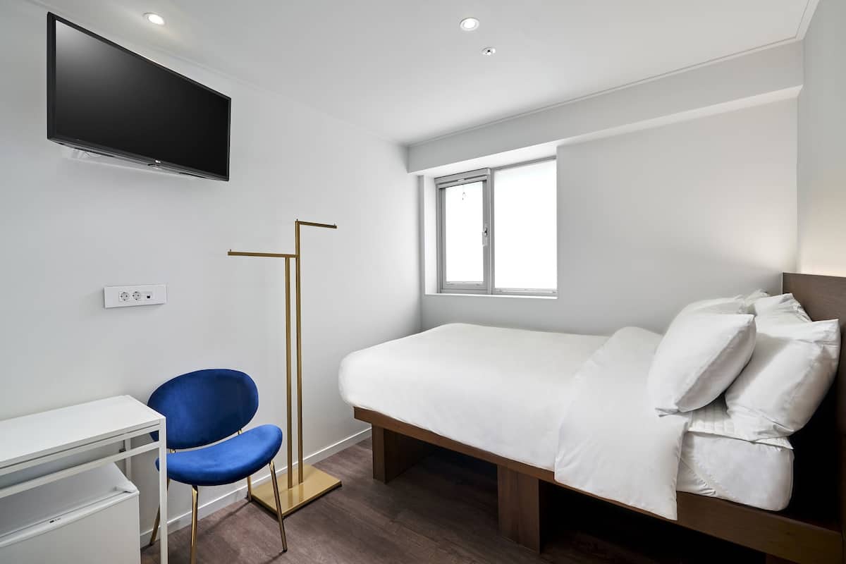 Una habitación de hotel con cama, escritorio, silla, televisor y ventana.