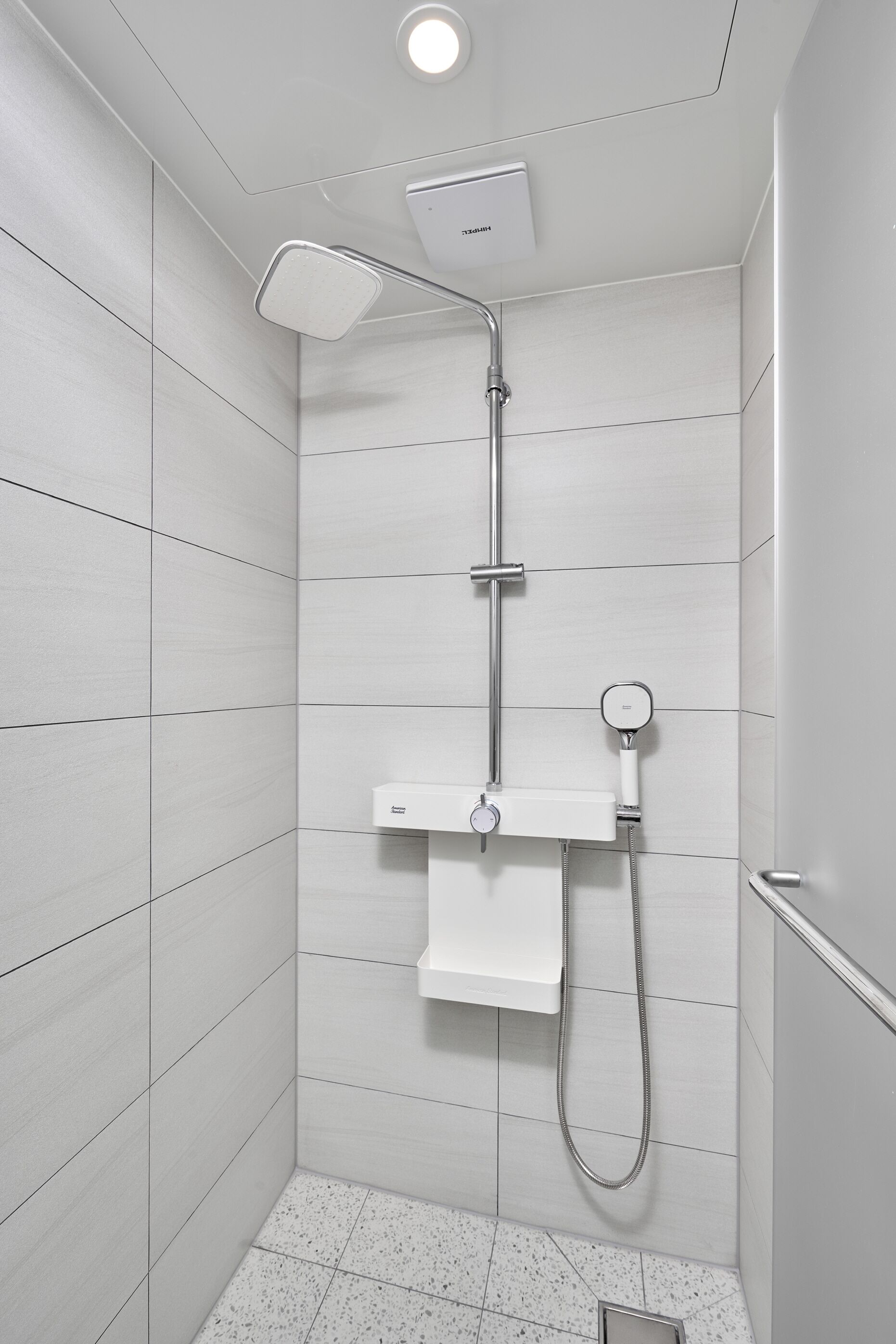 A modern shower with a handheld showerhead, a wall-mounted control panel, and a towel rack.