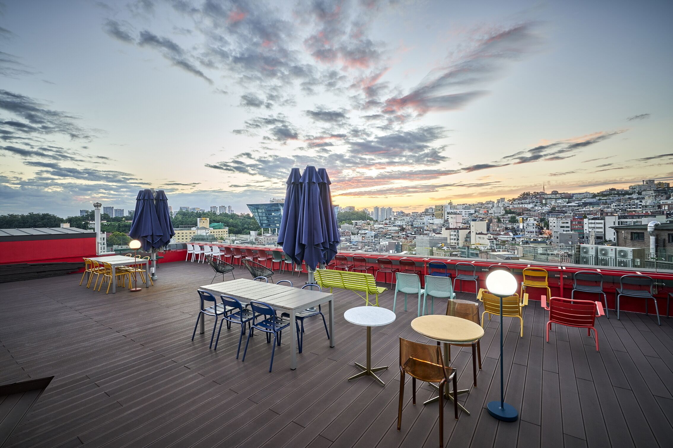 A rooftop terrace with tables and chairs, umbrellas, and a cityscape view.