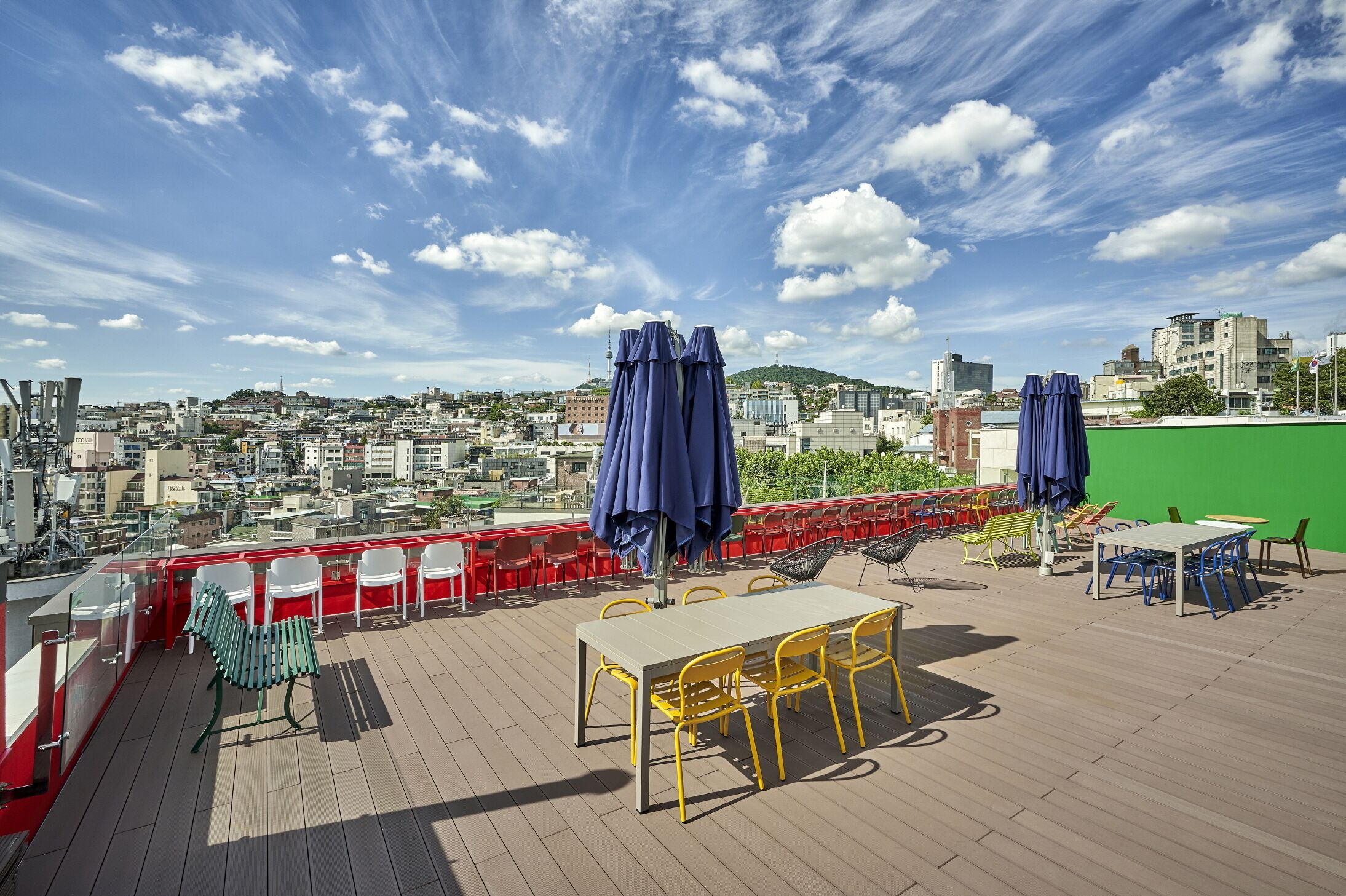 Eine Dachterrasse mit Sitzgelegenheiten im Freien, Blick auf die Stadt und einem grünen Hintergrund.
