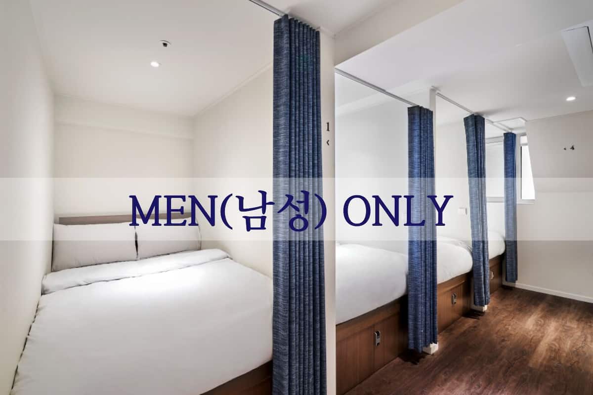 Baño de caballeros con cama, piso de madera y cortinas azules.