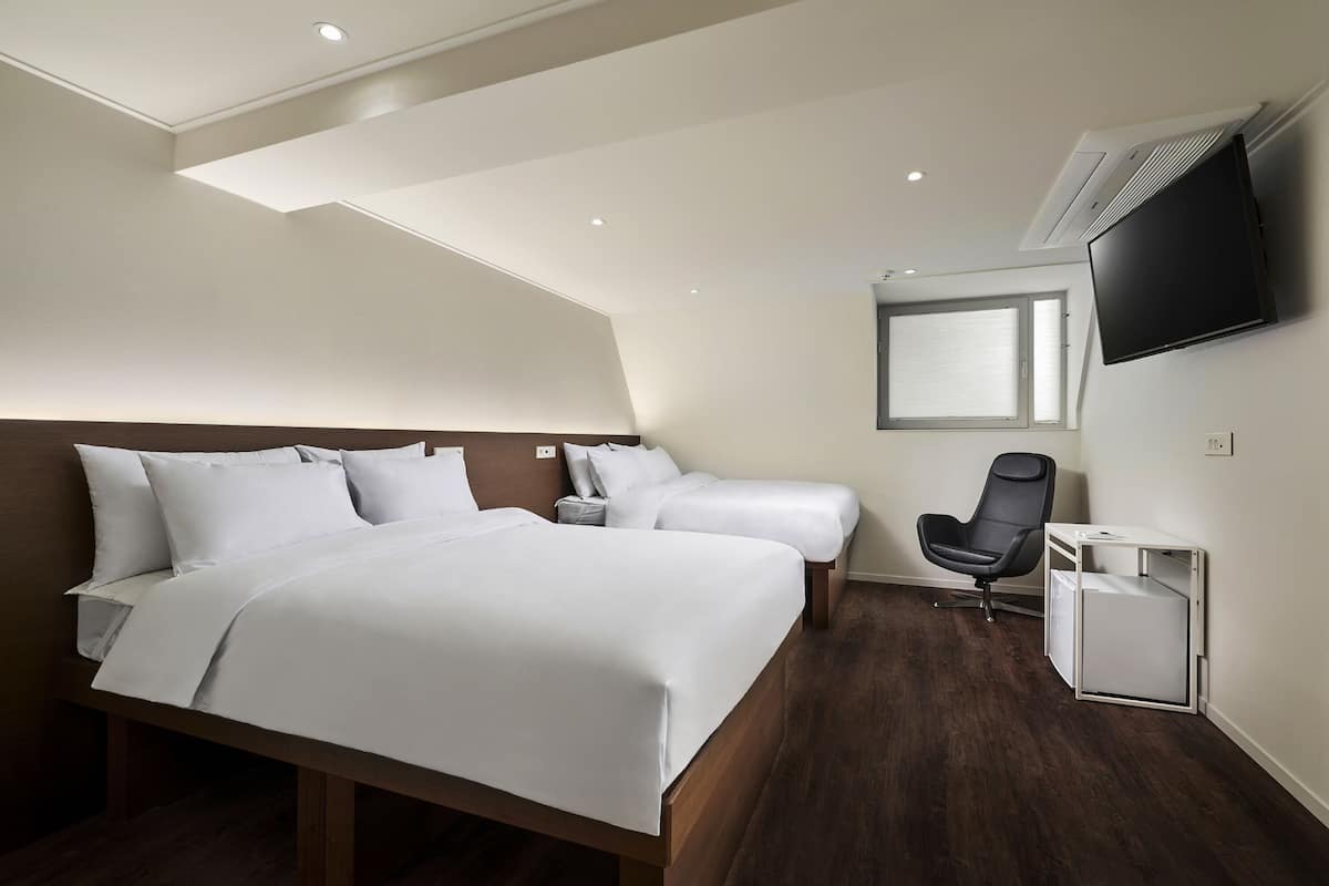 Habitación de hotel con una cama grande, dos mesitas de noche, una silla, un televisor y una ventana.