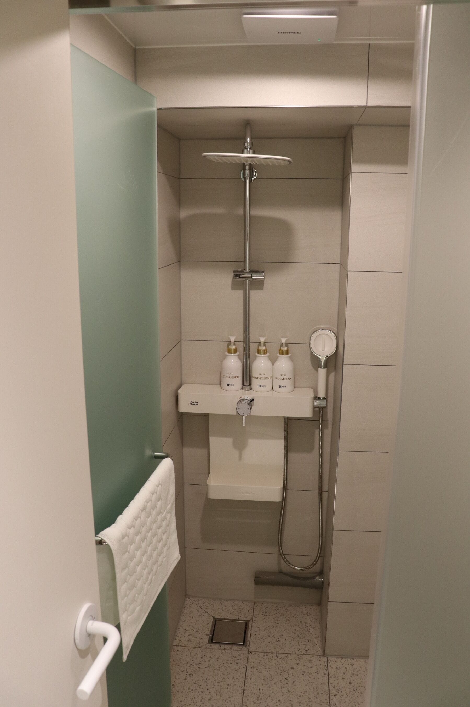 Un bagno compatto con doccia, asciugamano e ripiano con articoli da toilette.