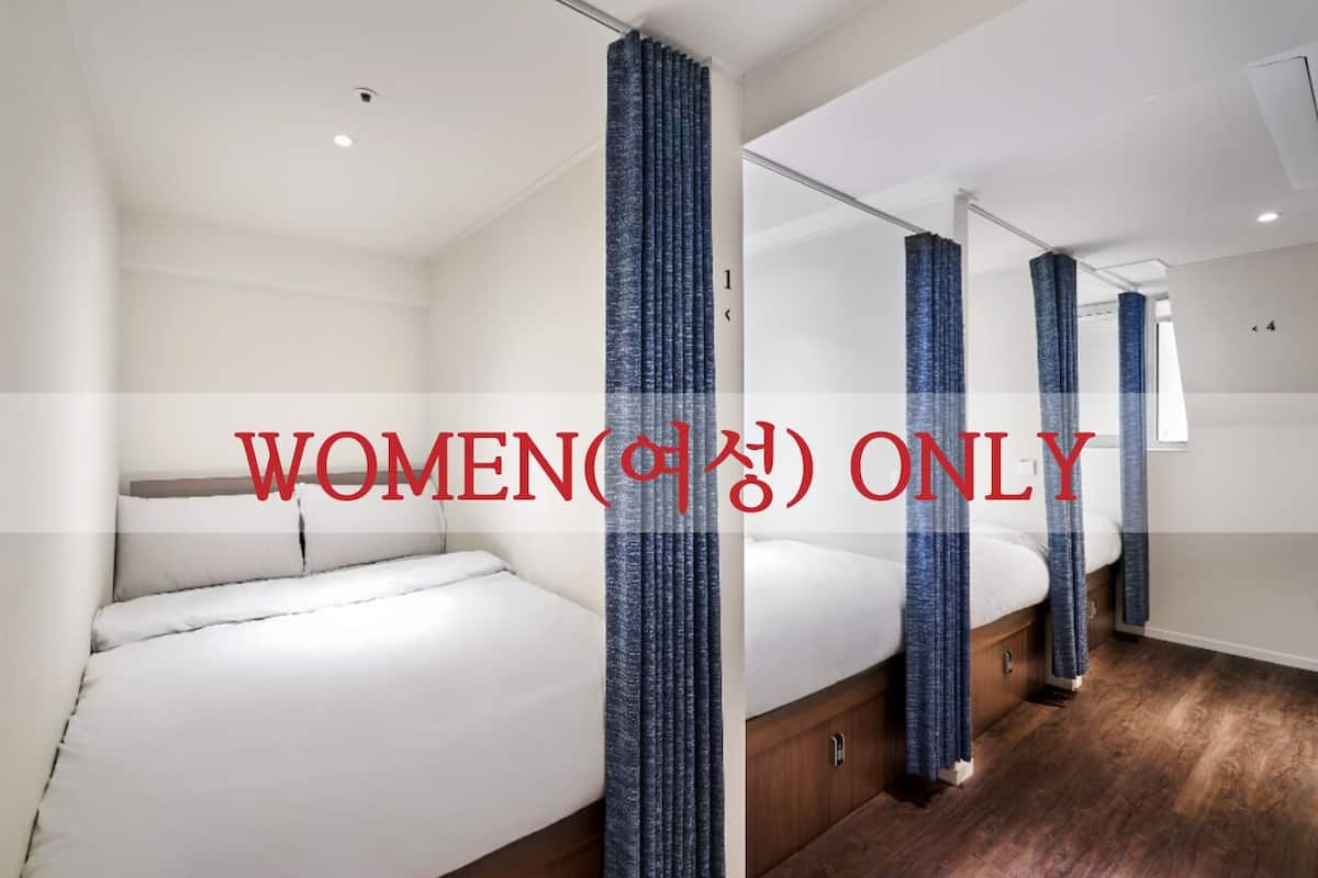 Un cuarto de mujeres con una cama, cortinas y piso de madera.