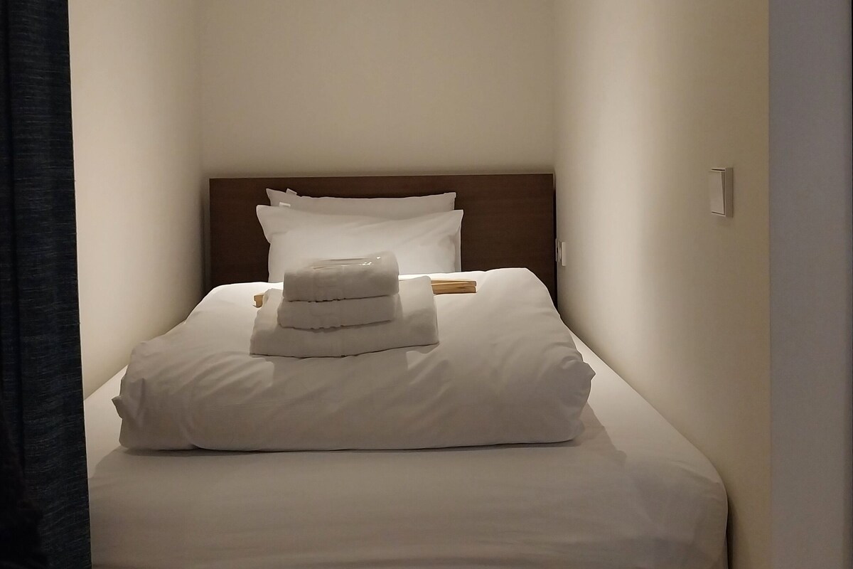 Una habitación de hotel con una cama bien hecha, un cabecero de madera y una mesita de noche pequeña.