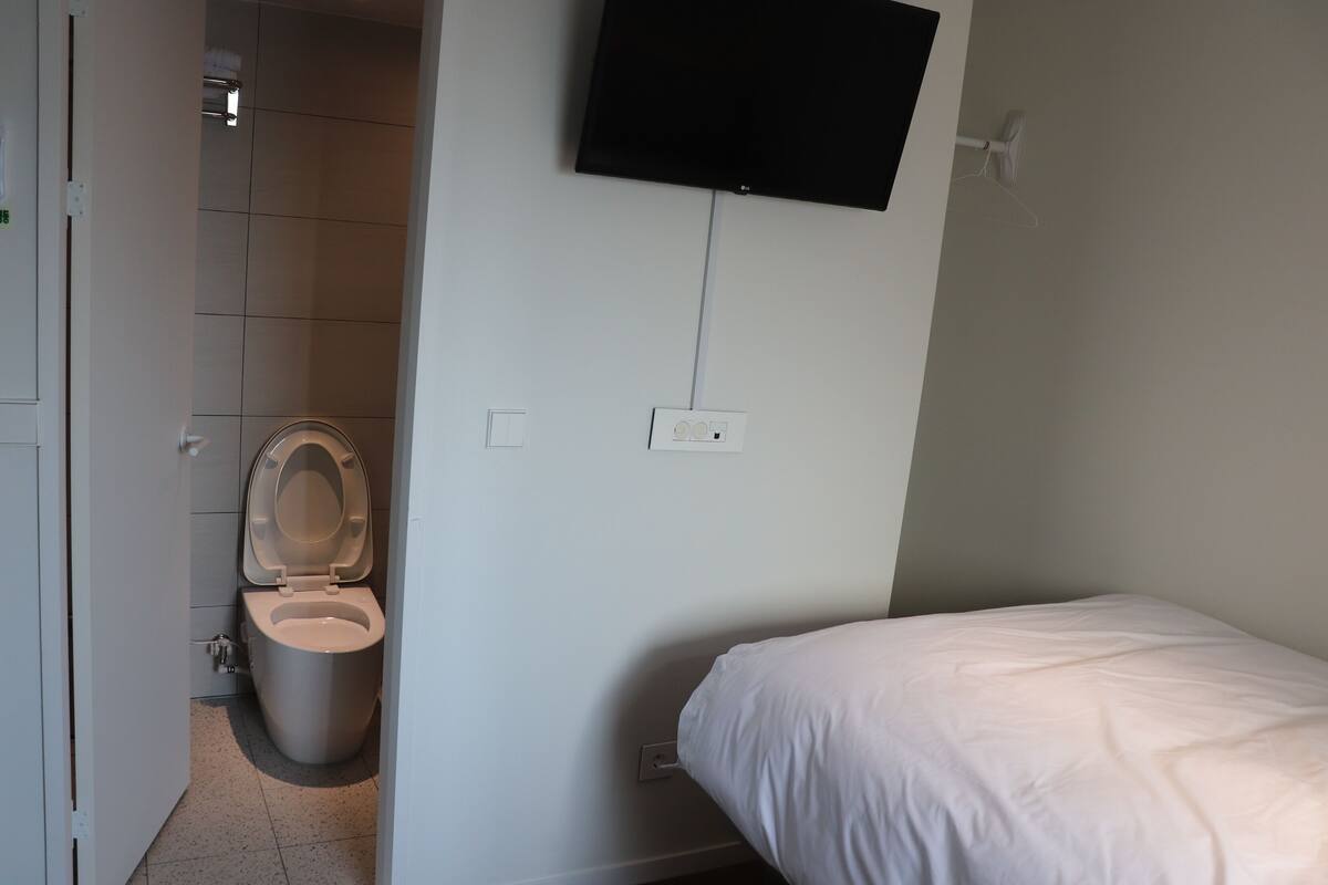 Una habitación de hotel con inodoro, cama y televisor montado.