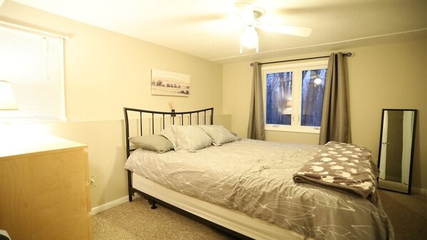Quarto com cama, janela com cortinas, ventilador de teto e mesa de cabeceira.