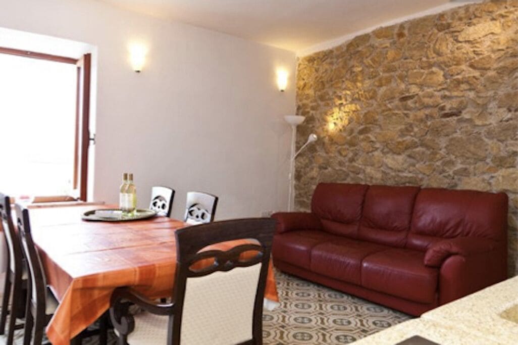 Un'area pranzo con tavolo e sedie in legno, una poltrona in pelle rossa e una parete in pietra.