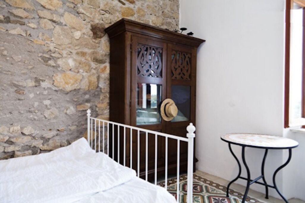 A room with a stone wall, a wooden cabinet with glass doors, a white bed, and a small round table.