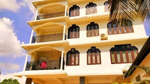 Un edificio de varios pisos con balcones, un coche estacionado al frente y palmeras.