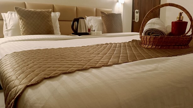 Una cama bien hecha con un edredón acolchado, una cesta de toallas y una cafetera sobre la mesita de noche.