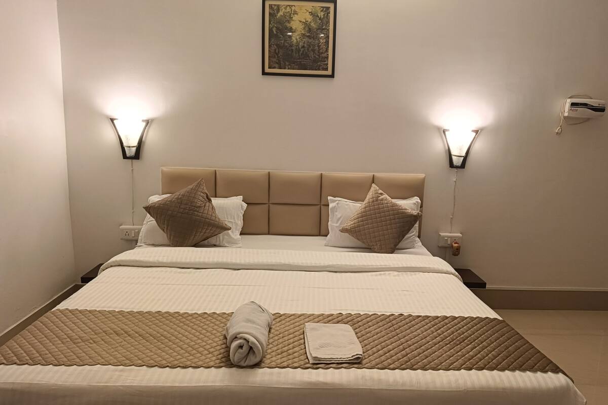 A neatly made bed with a beige headboard, two wall-mounted lights, and a framed picture on the wall.