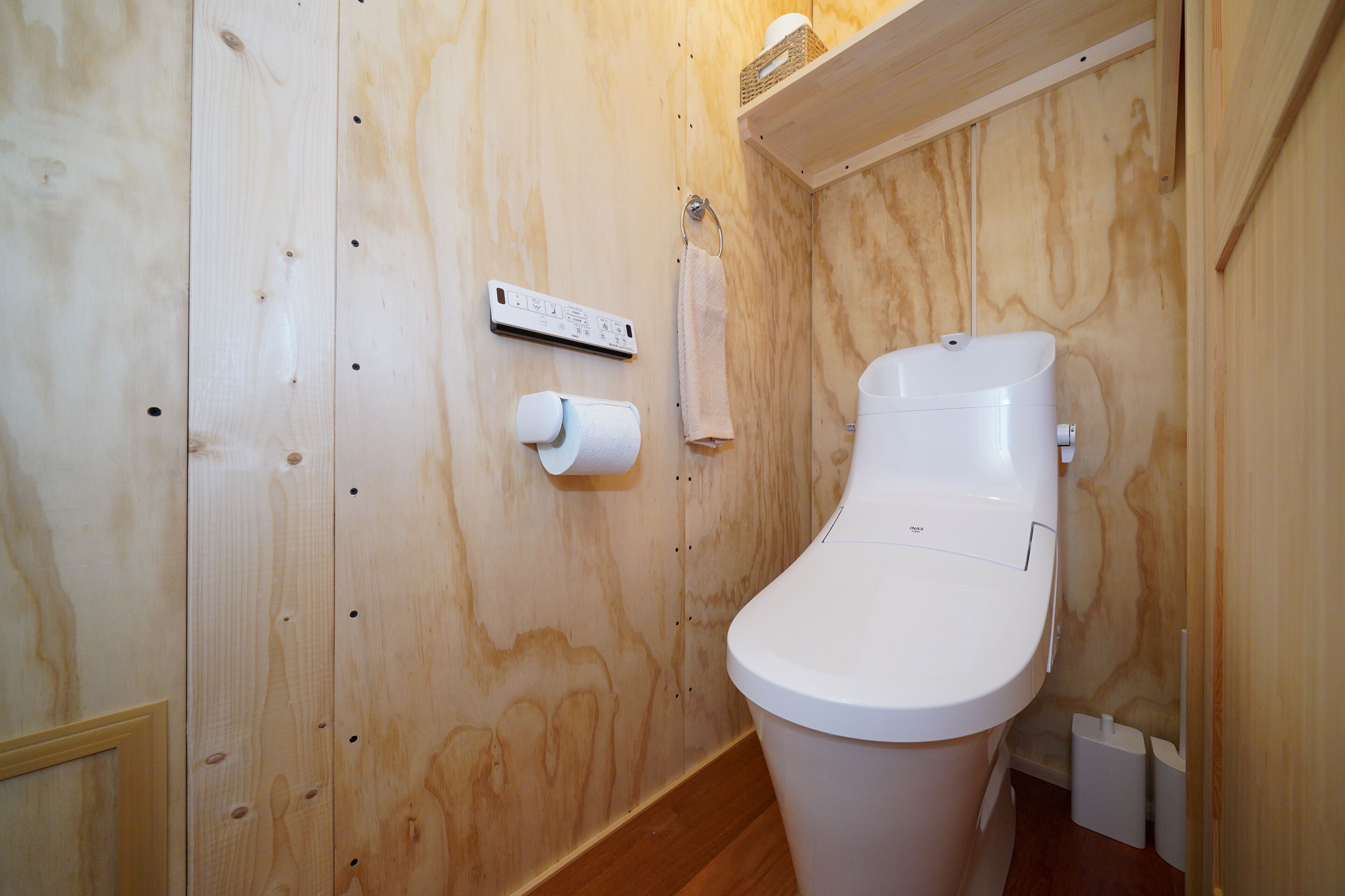 Un baño con paneles de madera, un inodoro blanco, un dispensador de toallas de papel y un rollo de papel higiénico.