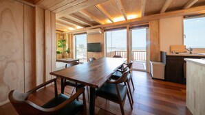Un interno in legno con un tavolo da pranzo, sedie, angolo cottura e ampie finestre.