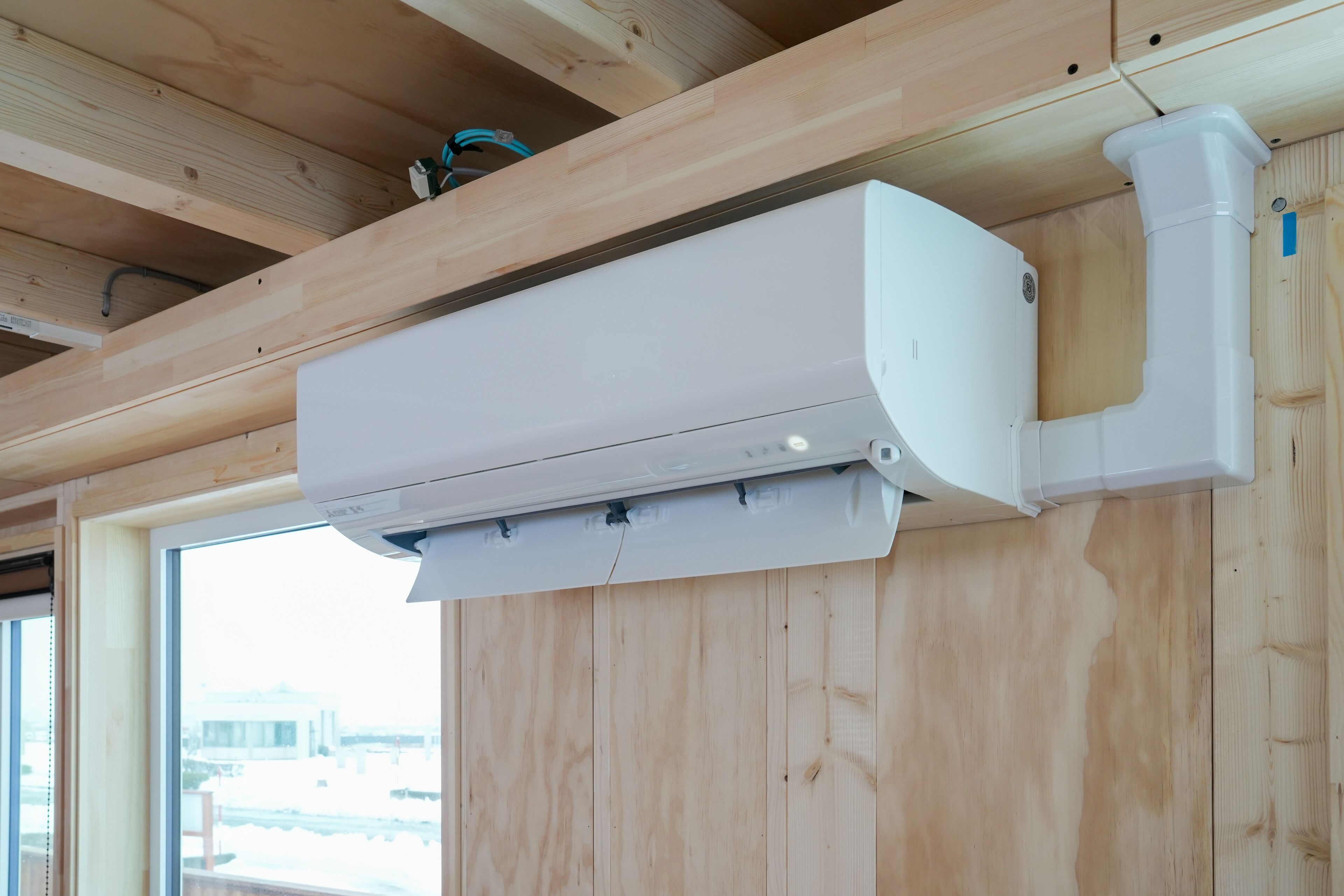 A white air conditioning unit mounted on a wooden ceiling with visible ductwork.