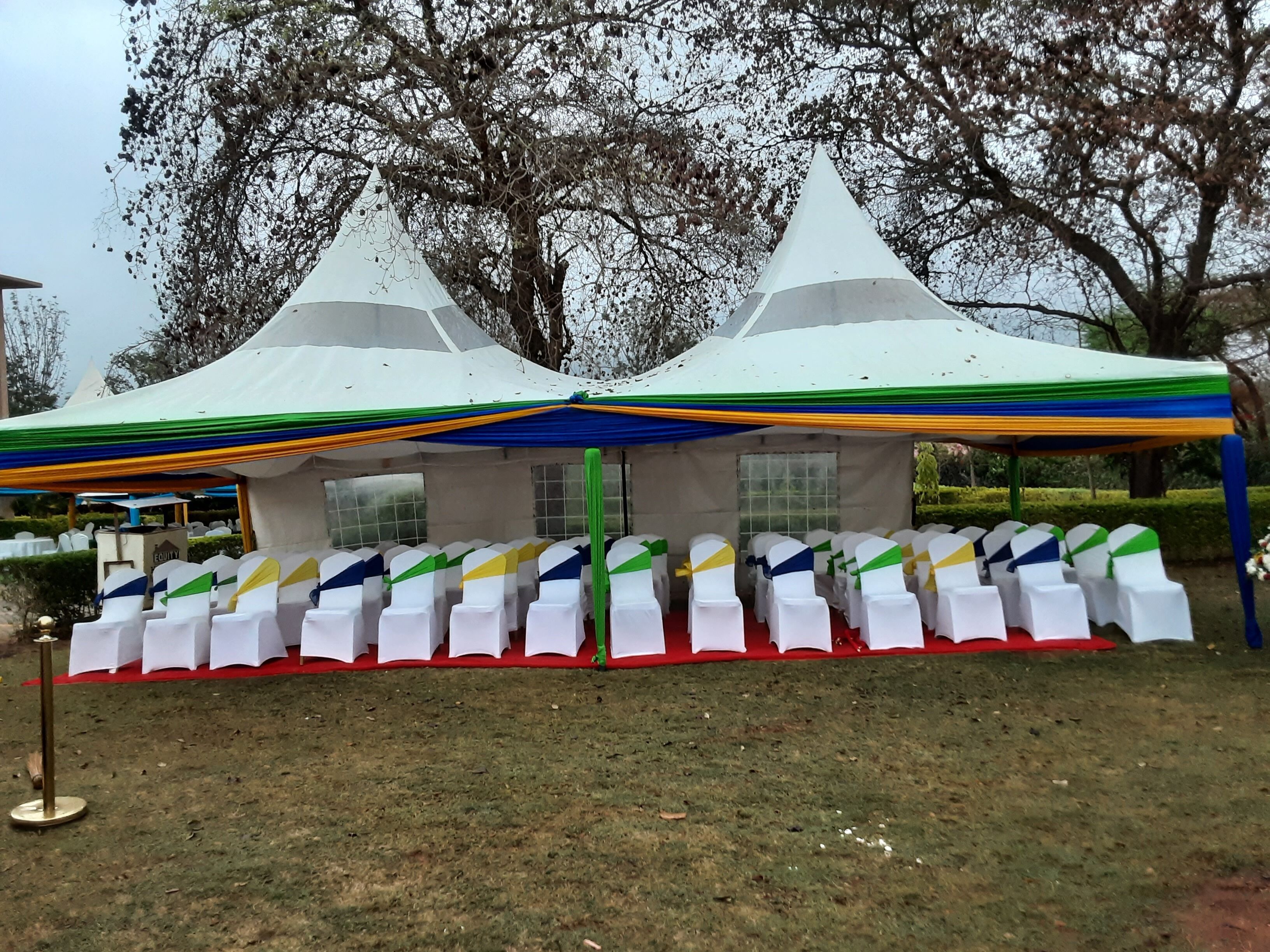 A tented event space with rows of white chairs, a red carpet, and a grassy area.