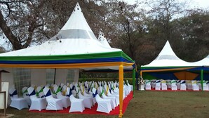 A tent with white chairs and a red carpet, surrounded by grass and trees. - THE BASE HOTEL (Mbooni)