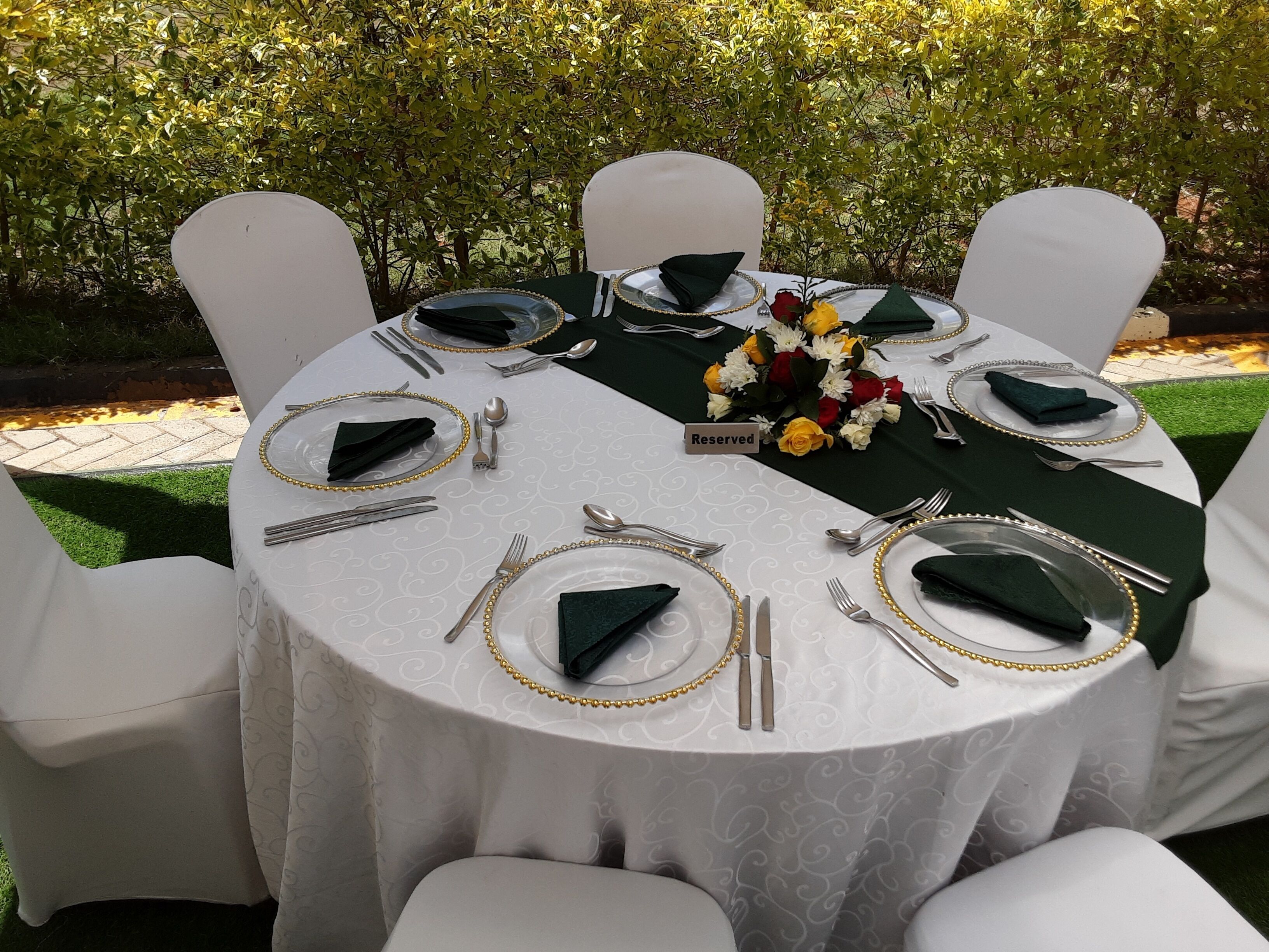 A round table set for six with white chairs, green napkins, and a floral centerpiece.