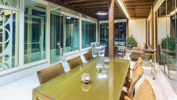 A spacious indoor area with a long wooden table, comfortable seating, and large windows offering views of the outside.