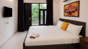 Ein Hotelzimmer mit einem Bett, einem Flachbildfernseher, einer Klimaanlage, einem Gemälde und einem Balkon mit Vorhängen.