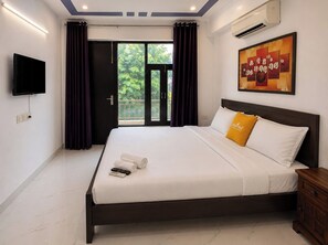 A hotel room with a bed, a flat-screen TV, an air conditioner, a painting, and a balcony with curtains. - Lime Tree 2Bhk Serviced Apartment (Gurugram)