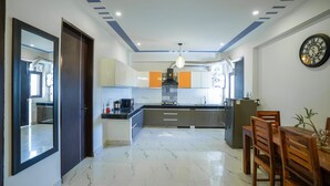A modern kitchen with a central island, a dining area with wooden chairs, and a wall-mounted clock. - Lime Tree 2Bhk Serviced Apartment (Gurugram)