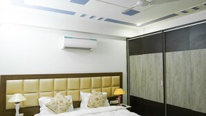 A hotel room with a bed, a nightstand, a lamp, an air conditioner, a ceiling fan, and a wardrobe. - Lime Tree 2Bhk Serviced Apartment (Gurugram)