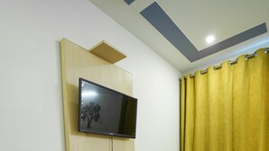 A living room with a mustard-colored sofa, a mounted flat-screen TV, and a yellow curtain. - Lime Tree 2Bhk Serviced Apartment (Gurugram)