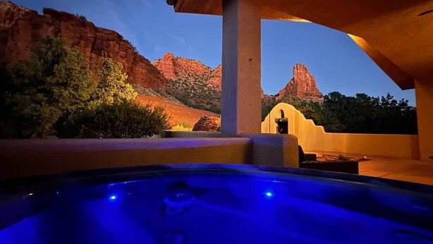 A hot tub with a blue light, a patio area, and a view of red rock formations.