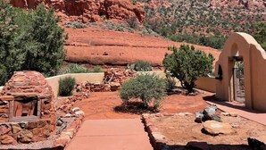 A rustic outdoor setting with a stone building, a pathway, and red rock formations in the background.