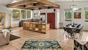 A spacious kitchen with a central island, wooden beams, large windows, and a dining area with a table and chairs.