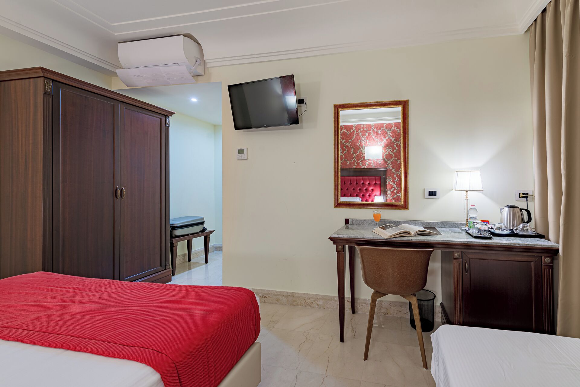 Una habitación de hotel con una cama, un escritorio con silla, un televisor, un espejo y una ventana con cortinas.