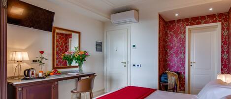A hotel room with a bed, a desk with a lamp, a mirror, a dresser, and a wardrobe.
