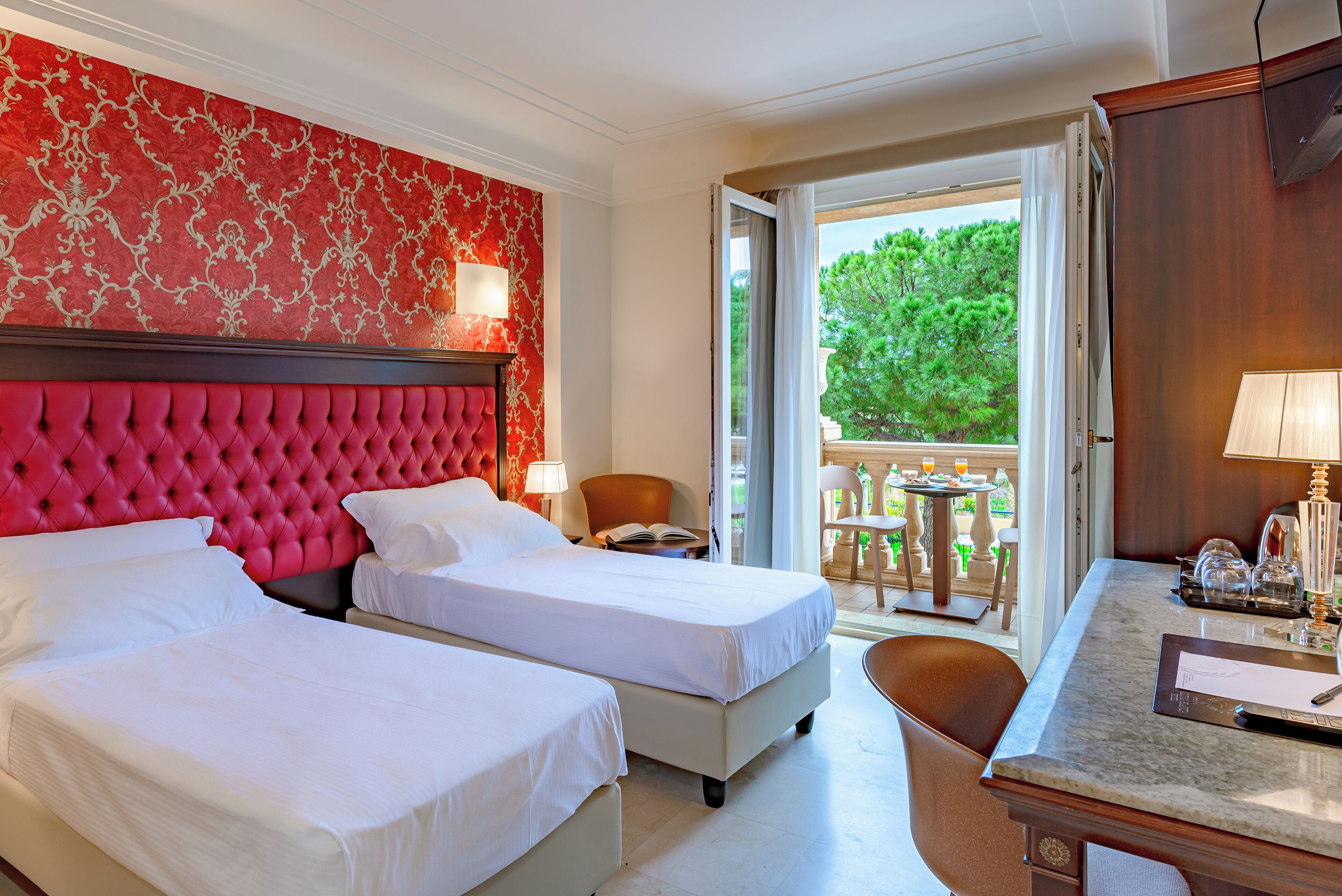 A hotel room with two beds, a desk, and a balcony with a table and chairs.