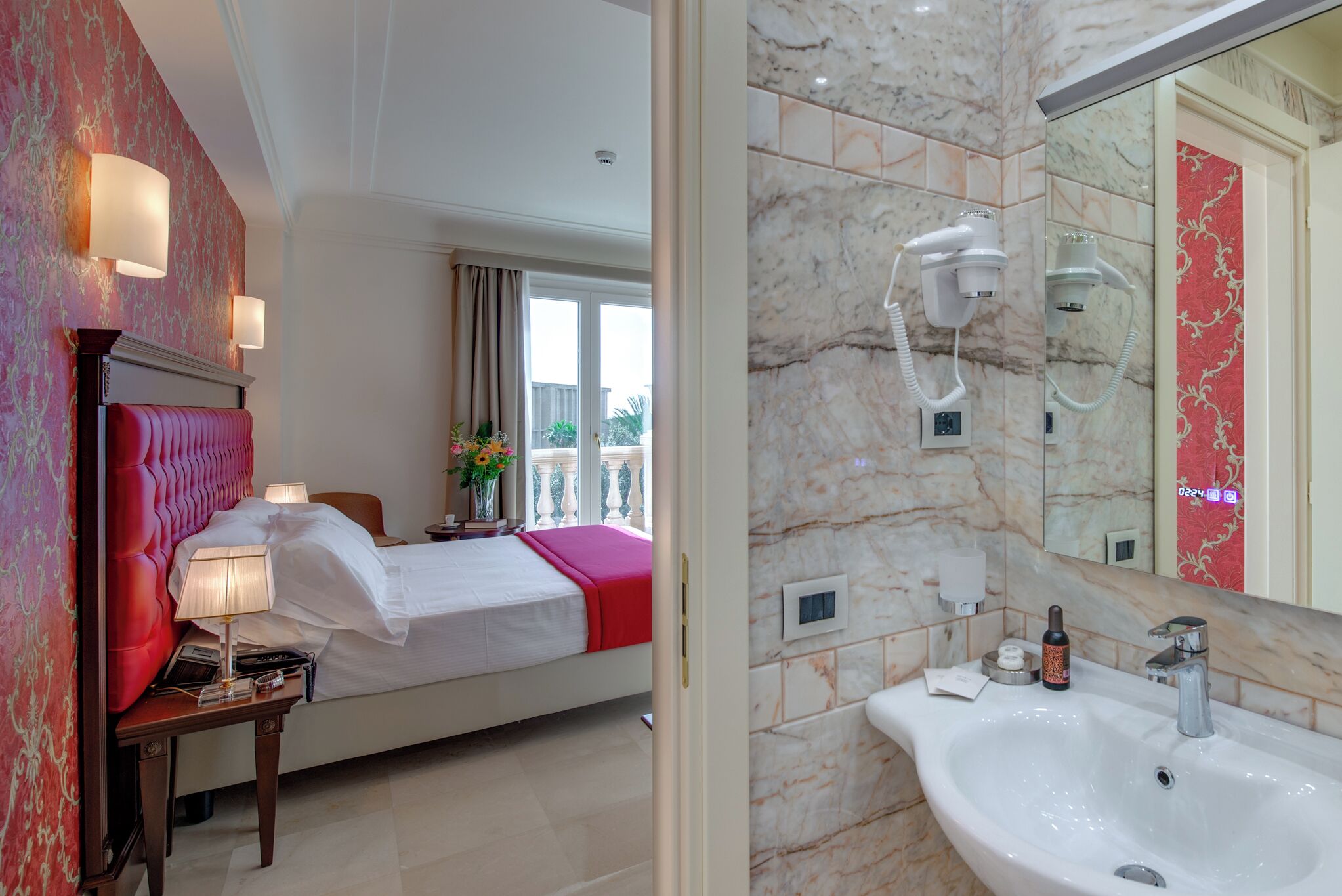 Une chambre d’hôtel comprenant un lit, une table de chevet, une lampe et une salle de bain avec un lavabo, un miroir et un sèche-cheveux.