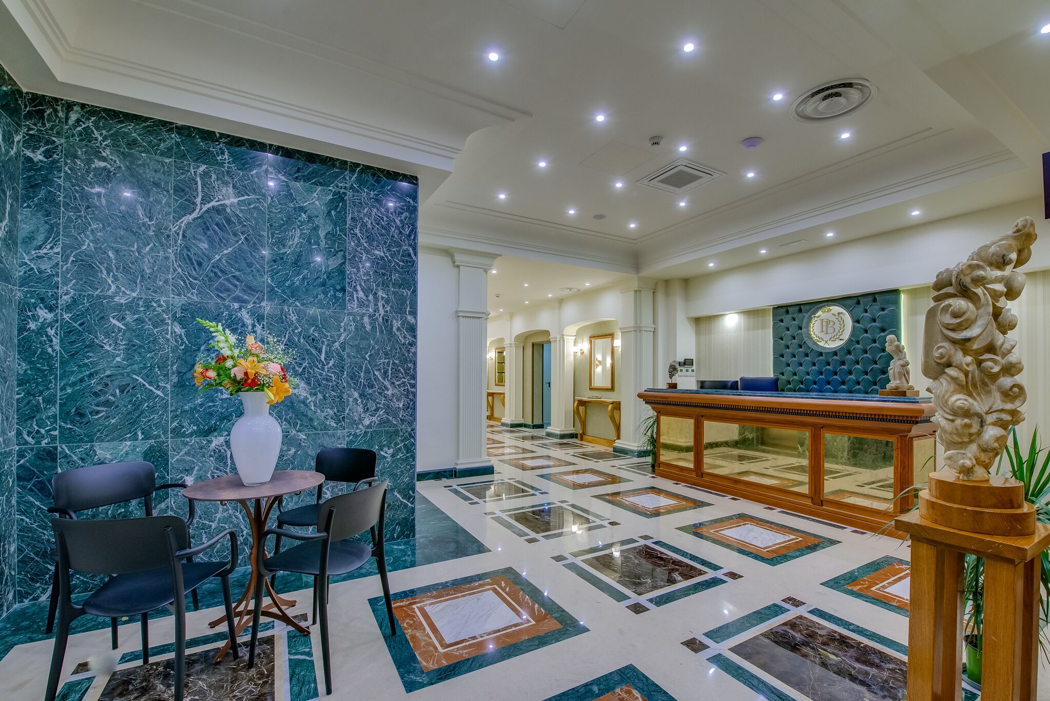 A lobby with a marble wall, a reception desk, and a seating area with chairs and a table.