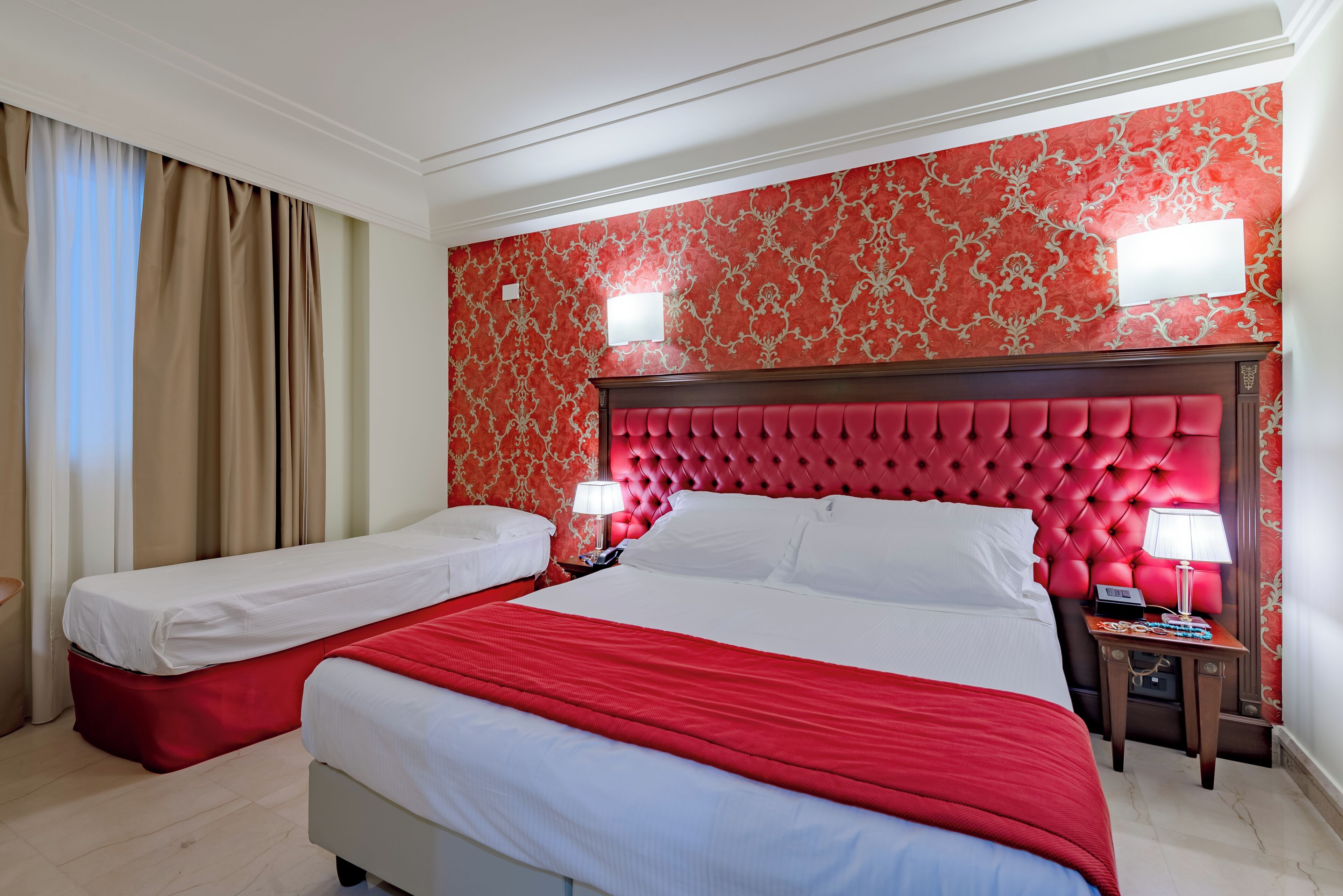 A hotel room with two beds, a red and white color scheme, and a patterned wallpaper.