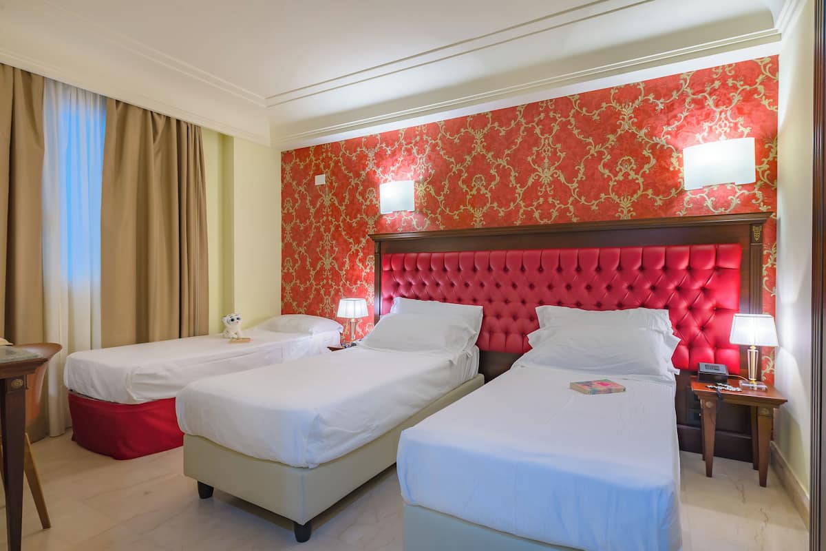 A hotel room with two single beds, a red headboard, and a patterned wallpaper.