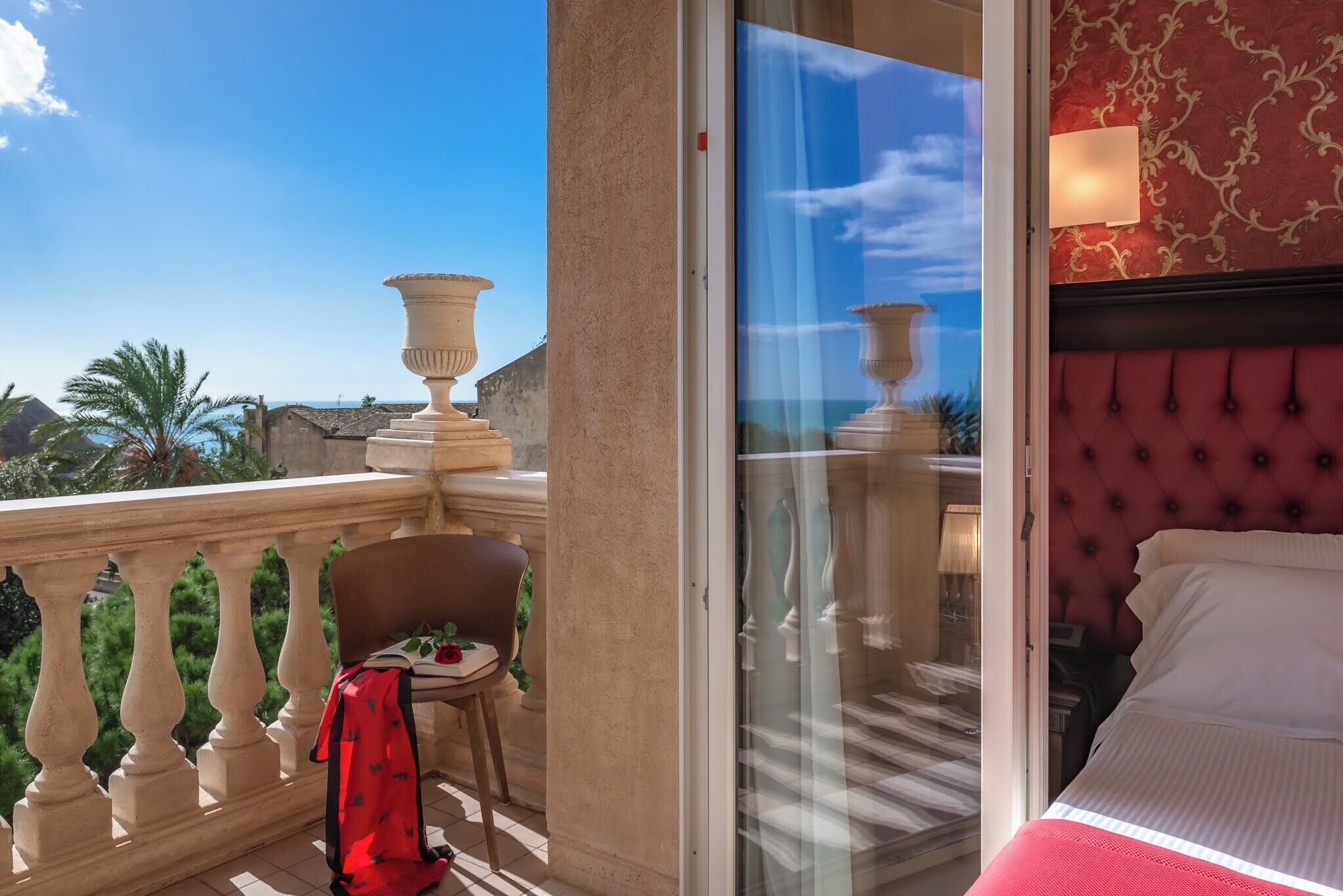 Une chambre d’hôtel avec balcon, un lit doté d’une tête de lit rouge et une vue sur la mer.